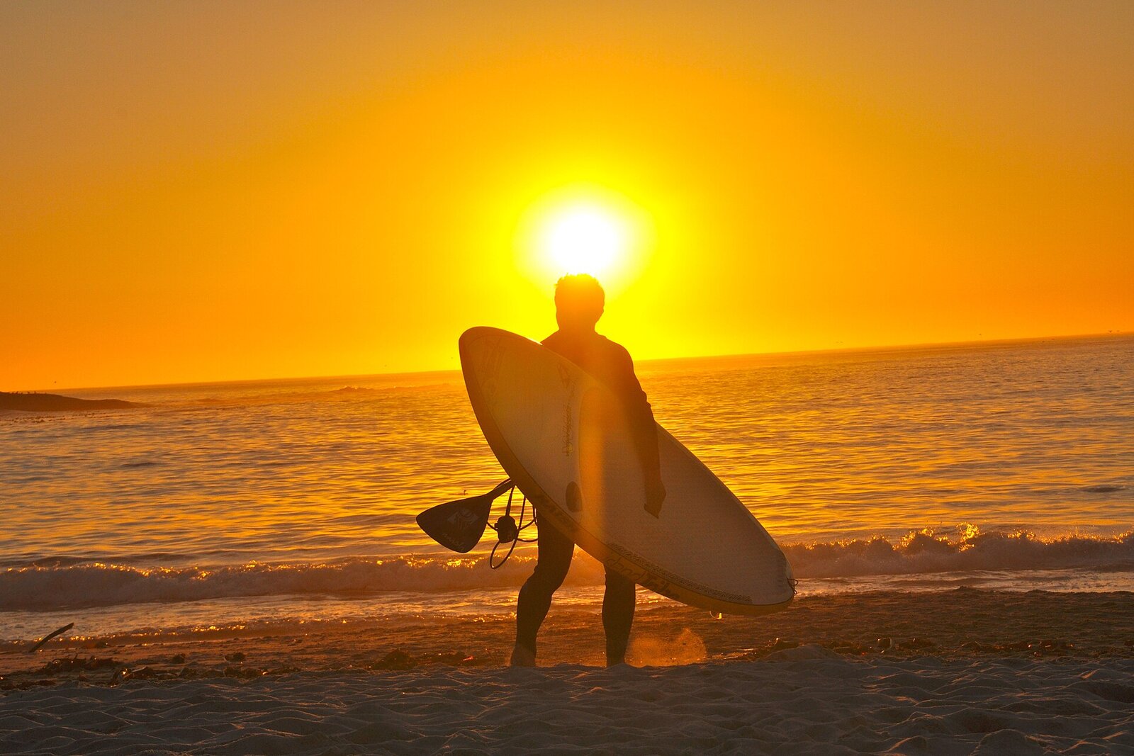Golden summer sunset over a Cape Town beach with a surfer walking the shoreline