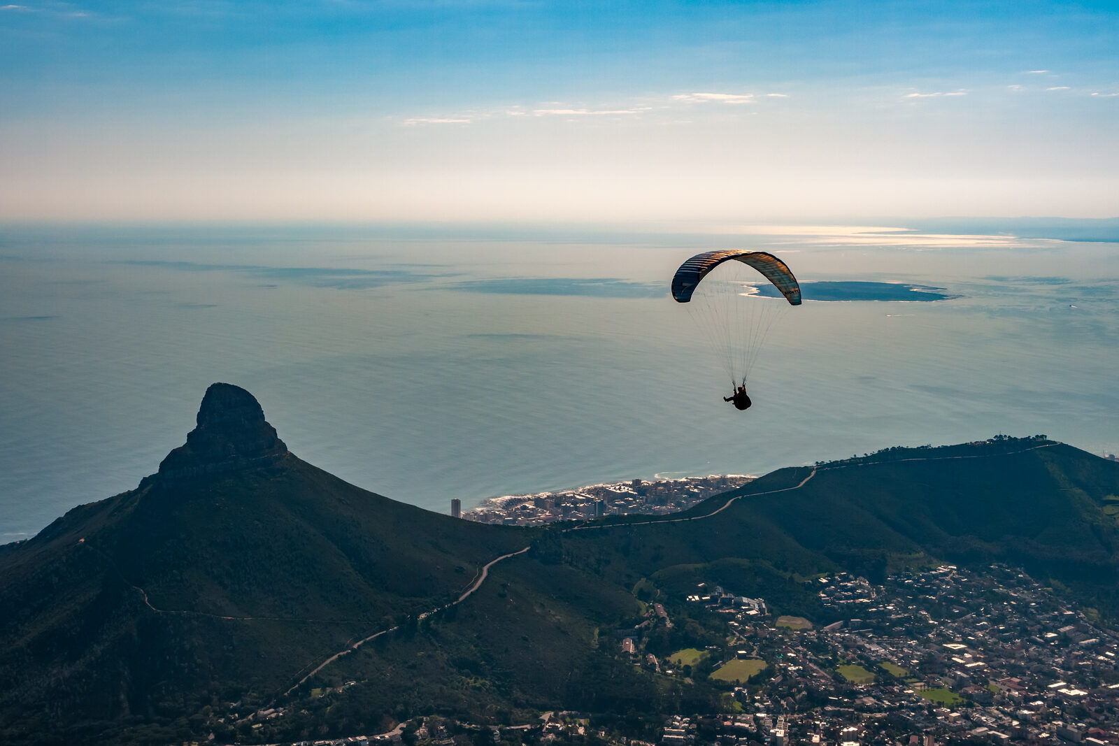 A paraglider soaring above Cape Town with Lions Head and the ocean below